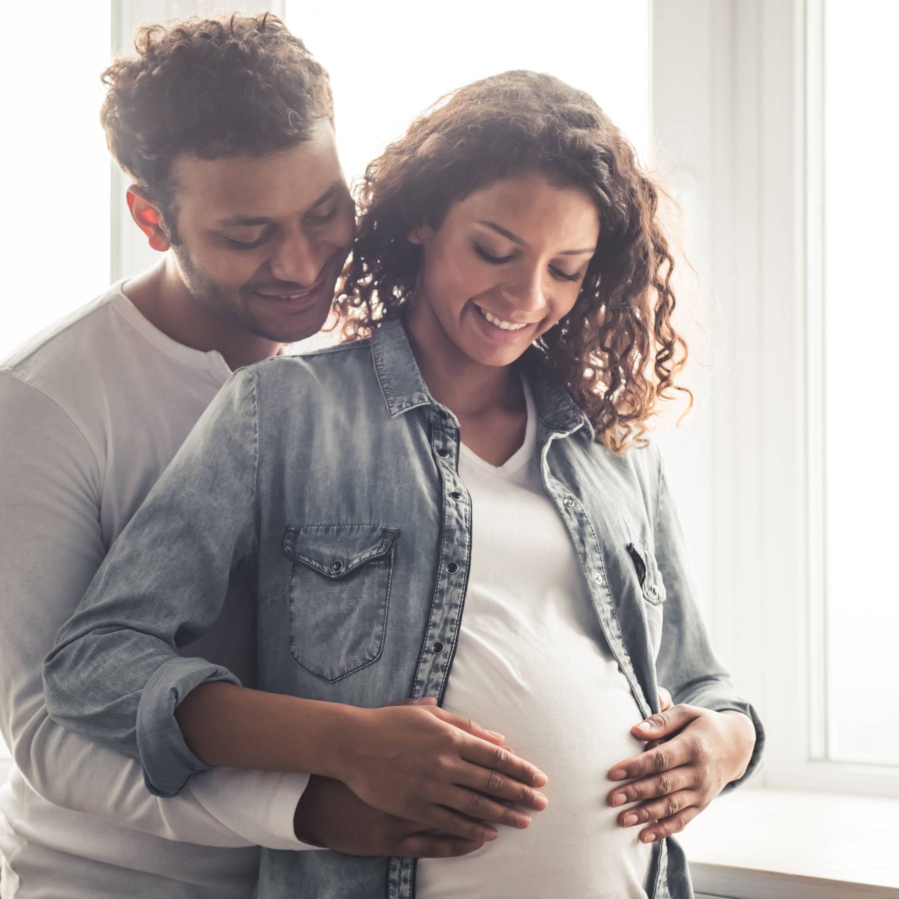 Man with arms around the stomach of pregnant female partner