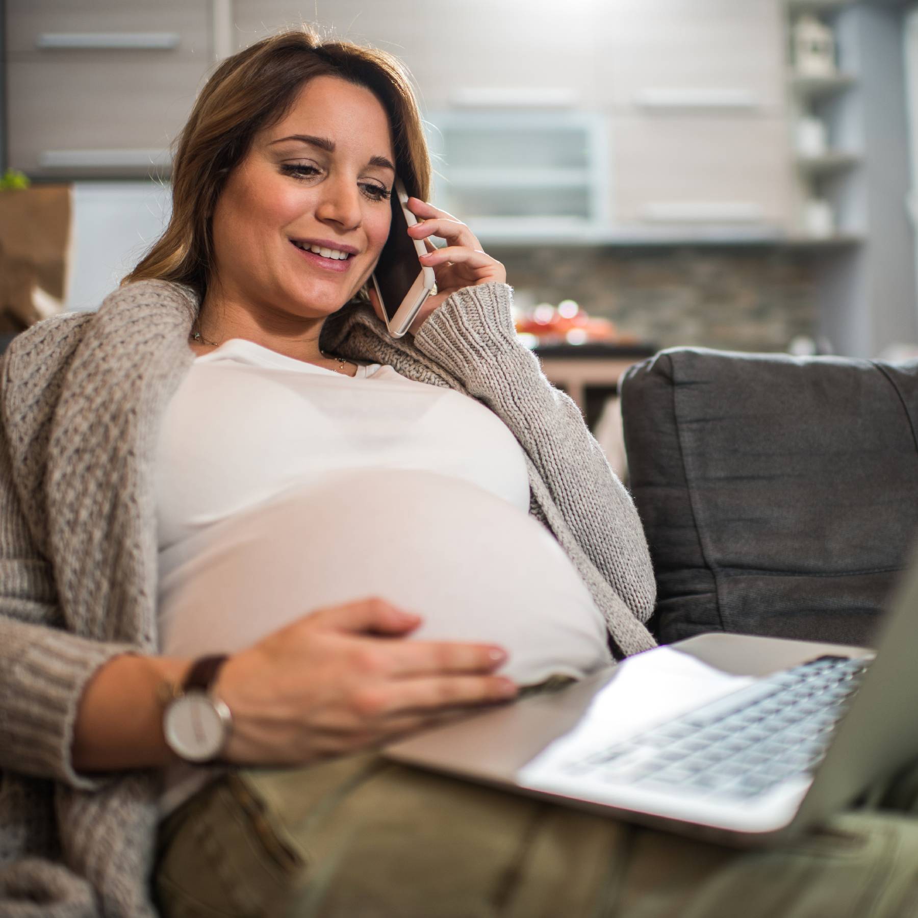 Pregnant female looking at laptop and talking on cell phone