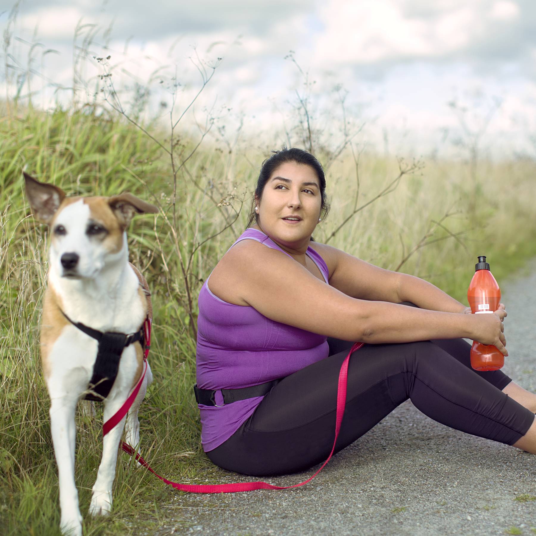 Woman sits on pavement after a run with dog by her side and water bottle in her hand.