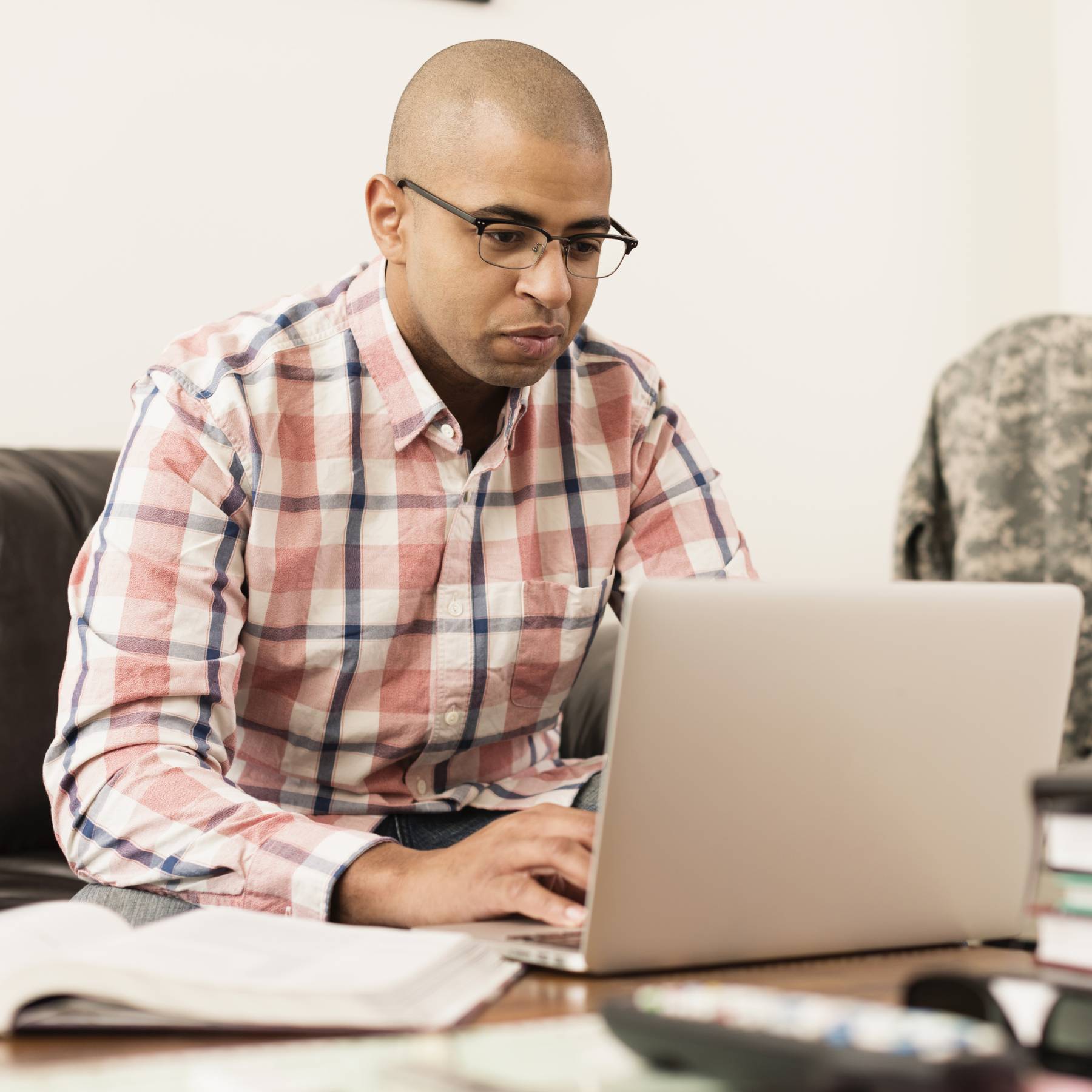 Man typing on laptop appears to be researching. He has a military jacket next to him.