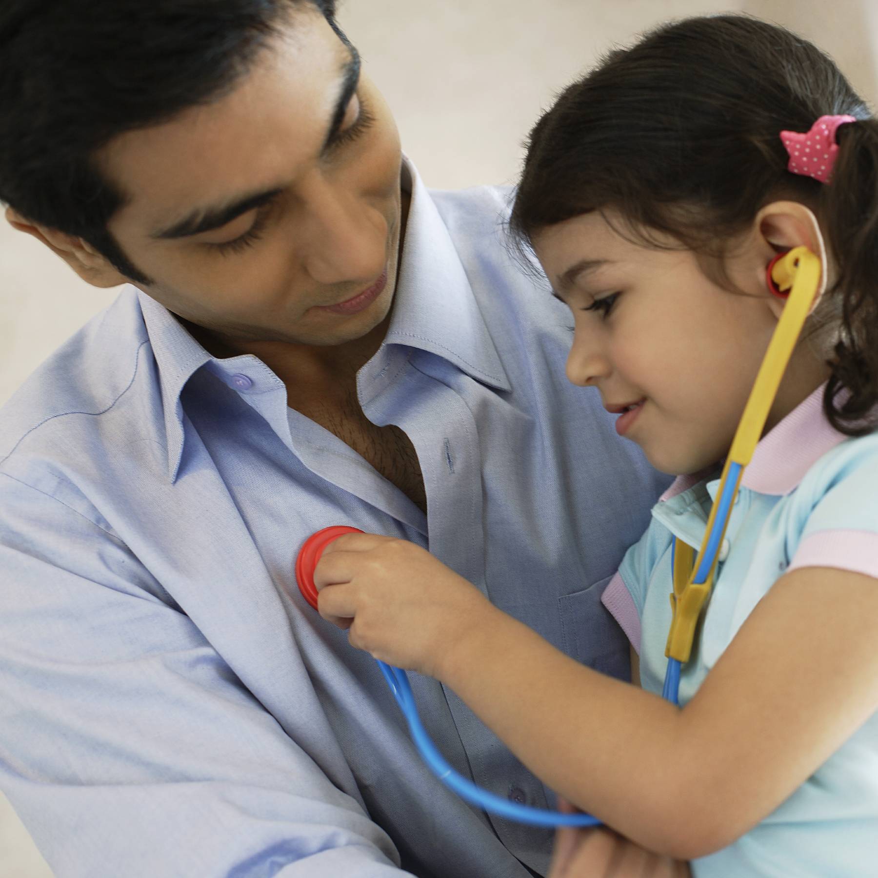 Young girl trying to listen to her father's heart with a toy stethescope.