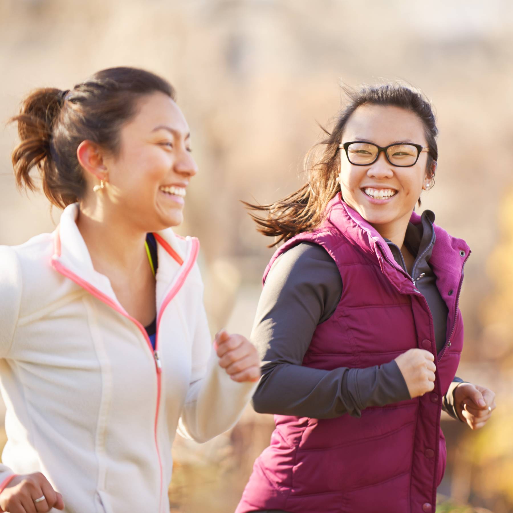 Two young women laughing while jogging outdoors.